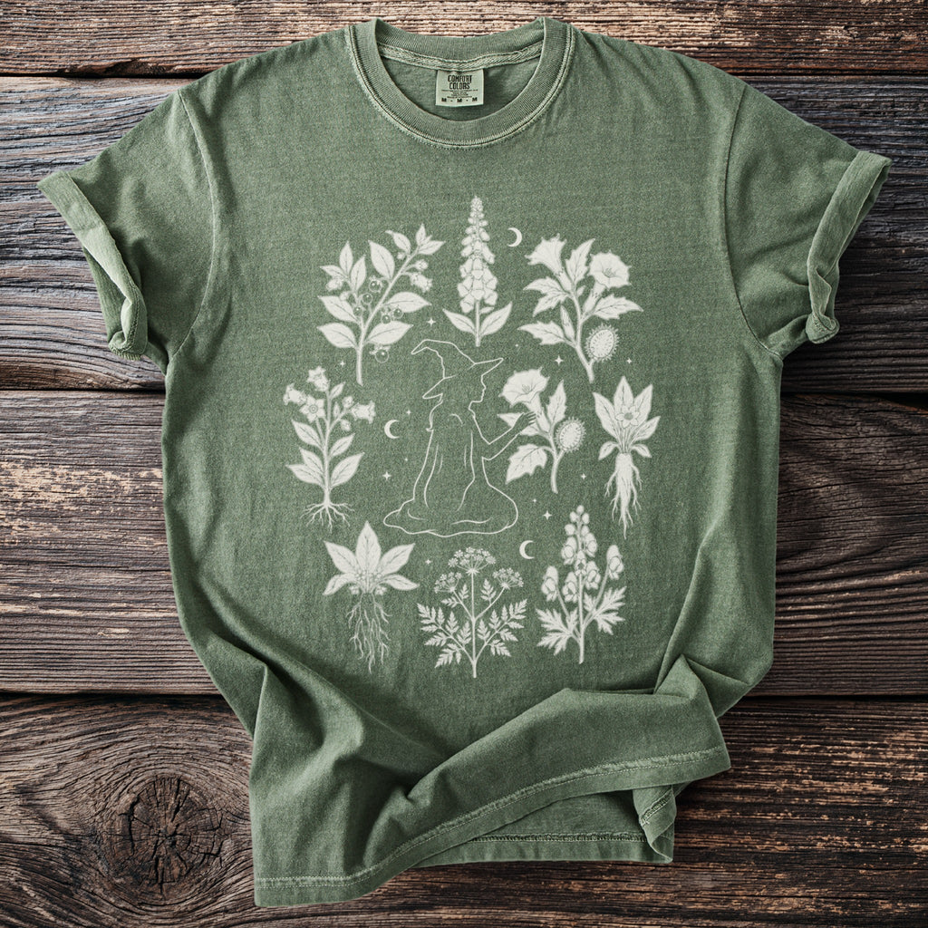 Green t-shirt with a white line drawing of a witch surrounded by botanical illustrations.