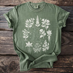 Green t-shirt with a white line drawing of a witch surrounded by botanical illustrations.