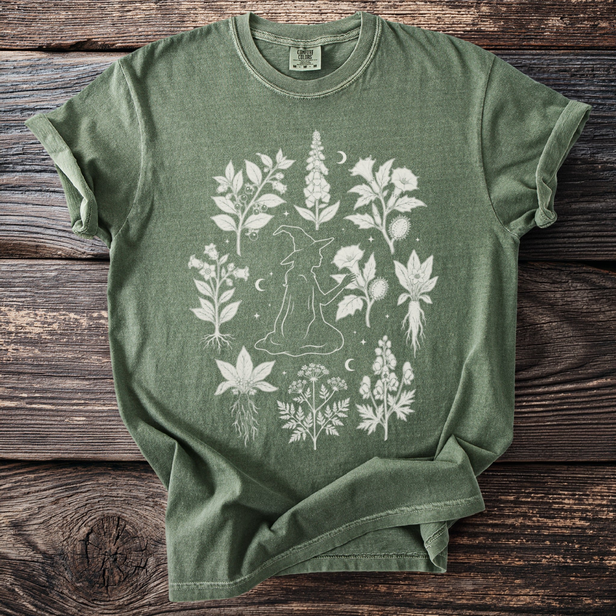 Green t-shirt with a white line drawing of a witch surrounded by botanical illustrations.