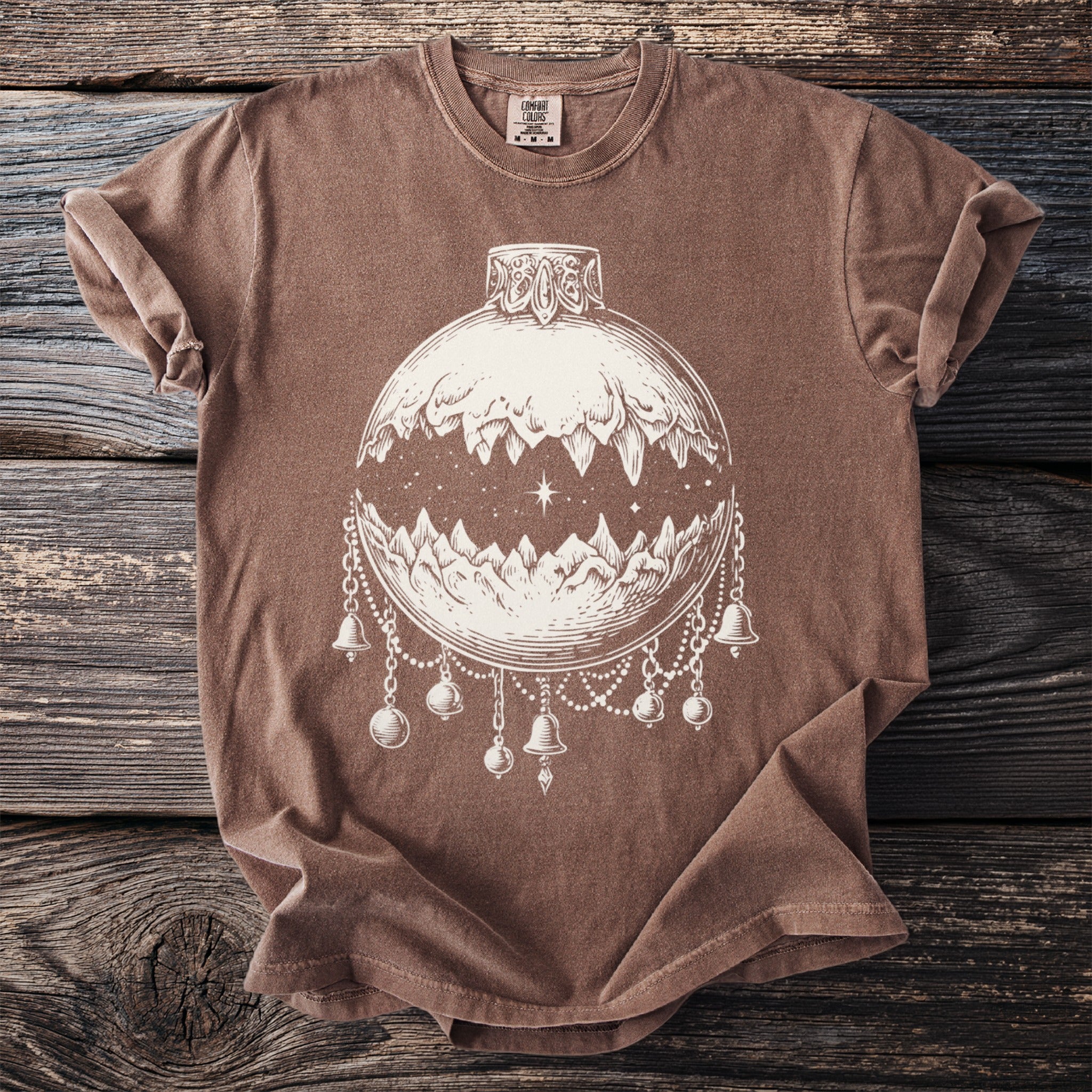 Brown t-shirt with cream line art of a mountain landscape inside an ornament.