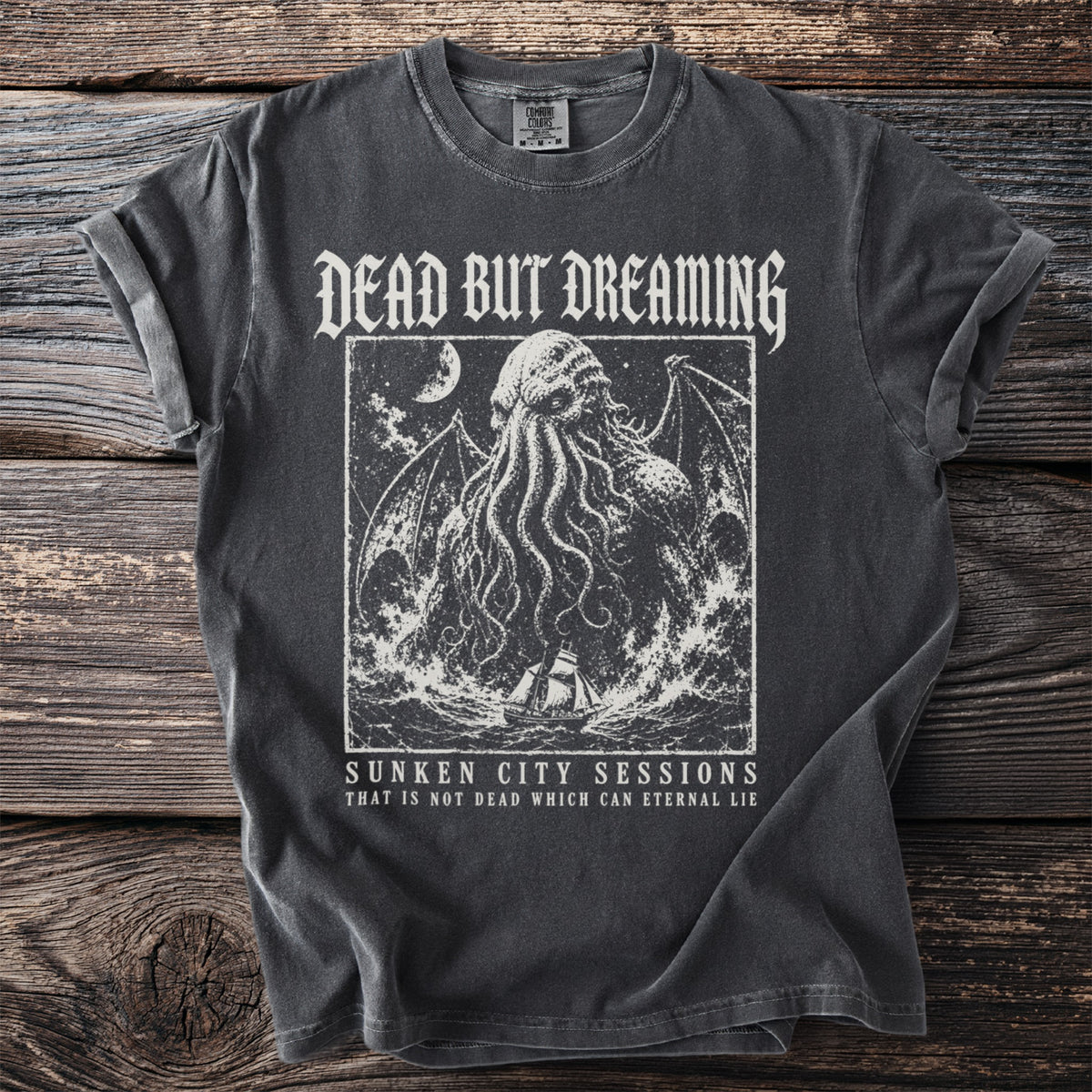 Dark grey t-shirt with a tentacled creature, ship, and text: Dead But Dreaming, Sunken City Sessions.