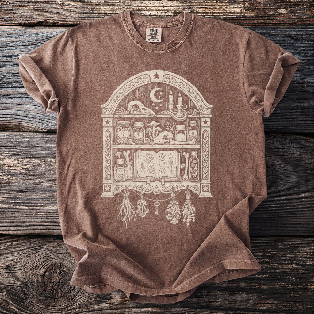 Brown t-shirt with a white graphic of a witch's apothecary shelf.