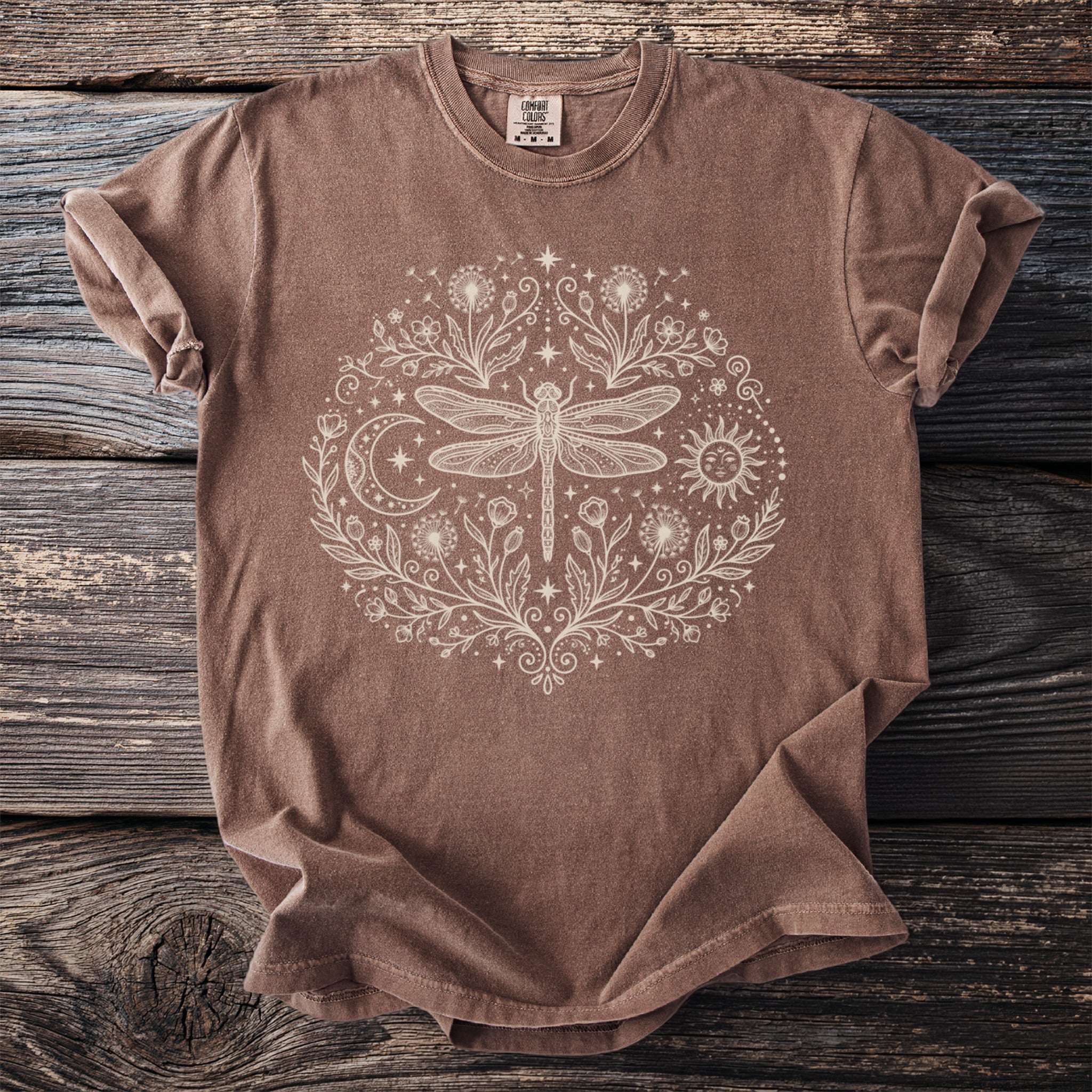 Brown t-shirt with circular dragonfly, sun, moon, and floral design.