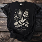Black t-shirt with botanical illustrations of Rooibos, Yerba Mate, Hibiscus, Roman Chamomile, Peppermint, and Tea Plant.