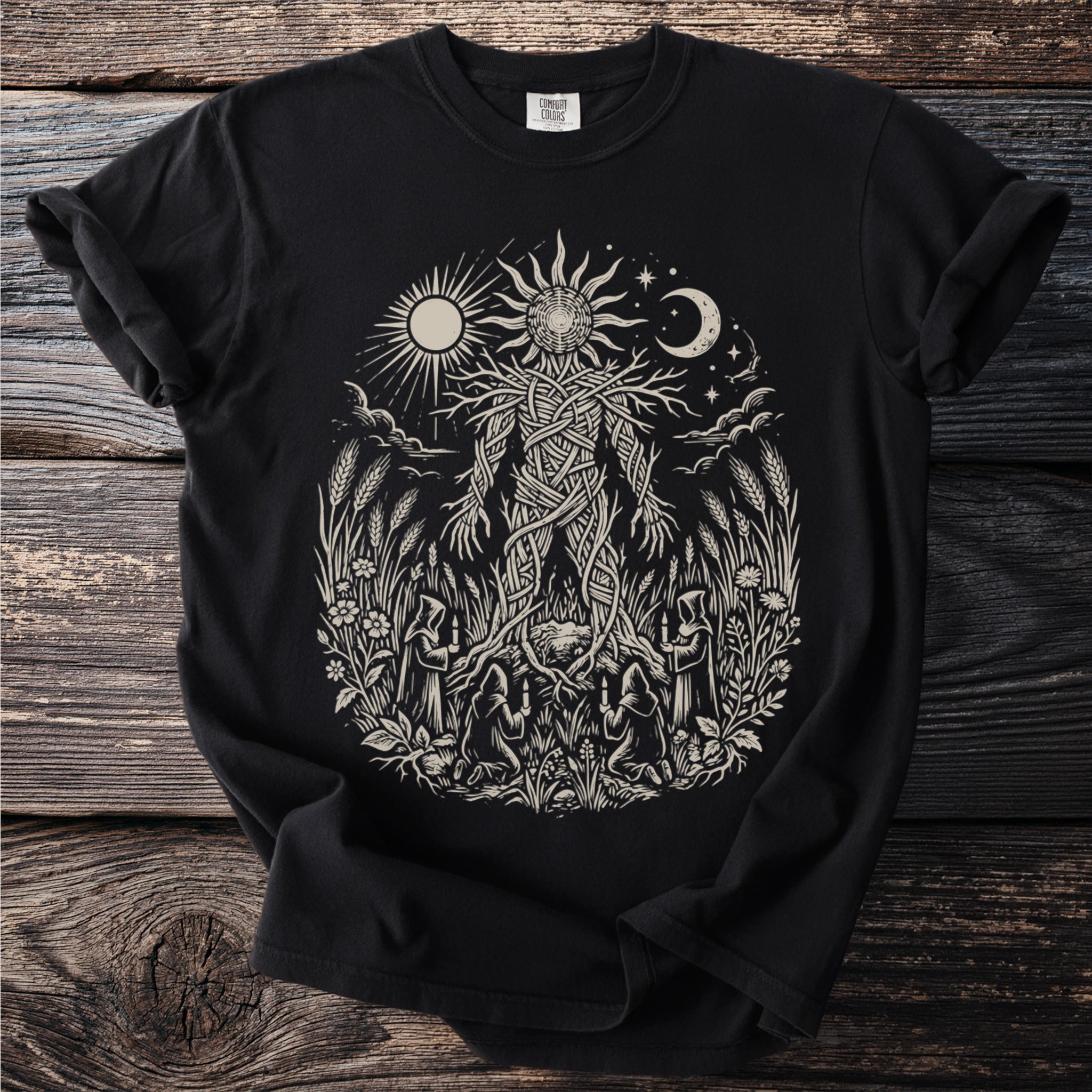 Black t-shirt with a cream linocut style print of a tree-like figure surrounded by nature scenes and figures.