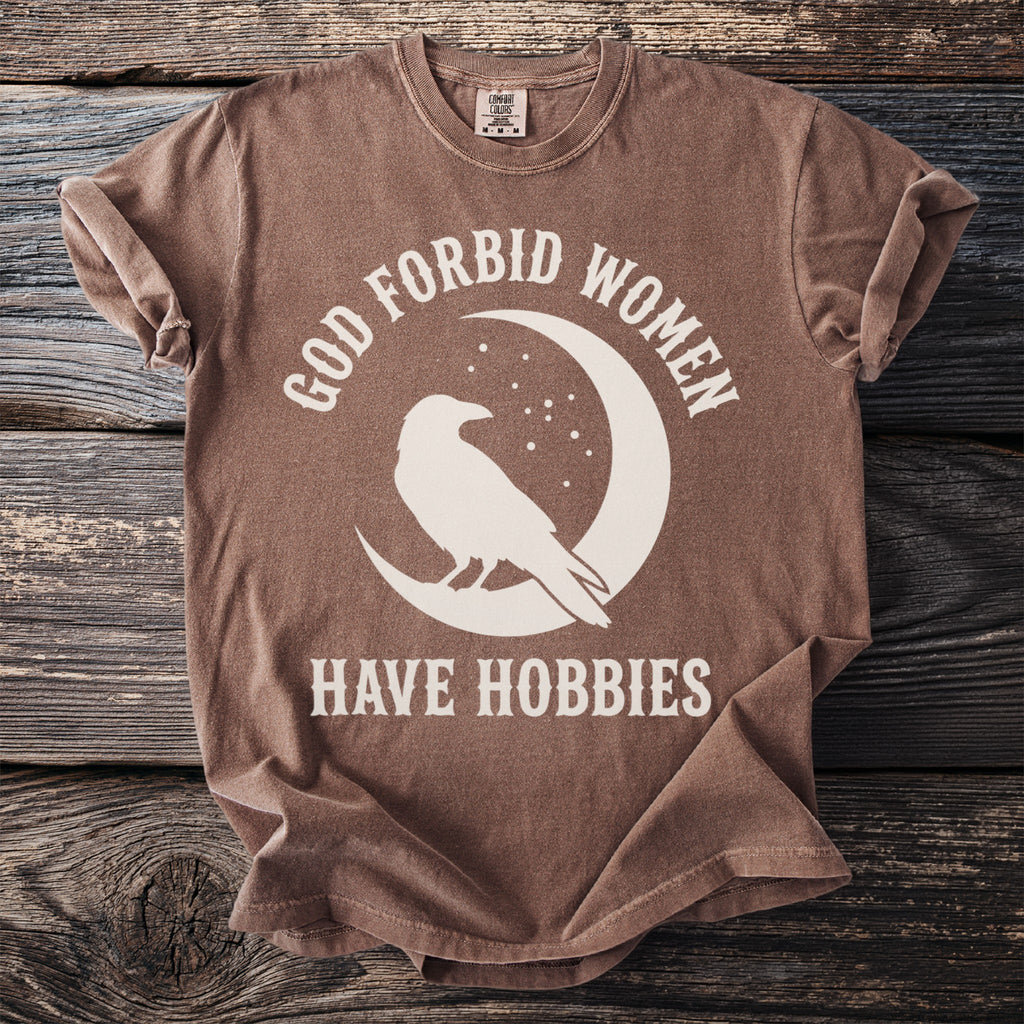 Brown t-shirt with white graphic of raven on moon, text "GOD FORBID WOMEN HAVE HOBBIES".