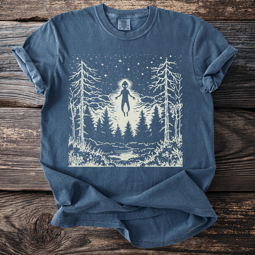 Blue t-shirt with a white graphic of an alien figure floating over a forest at night.
