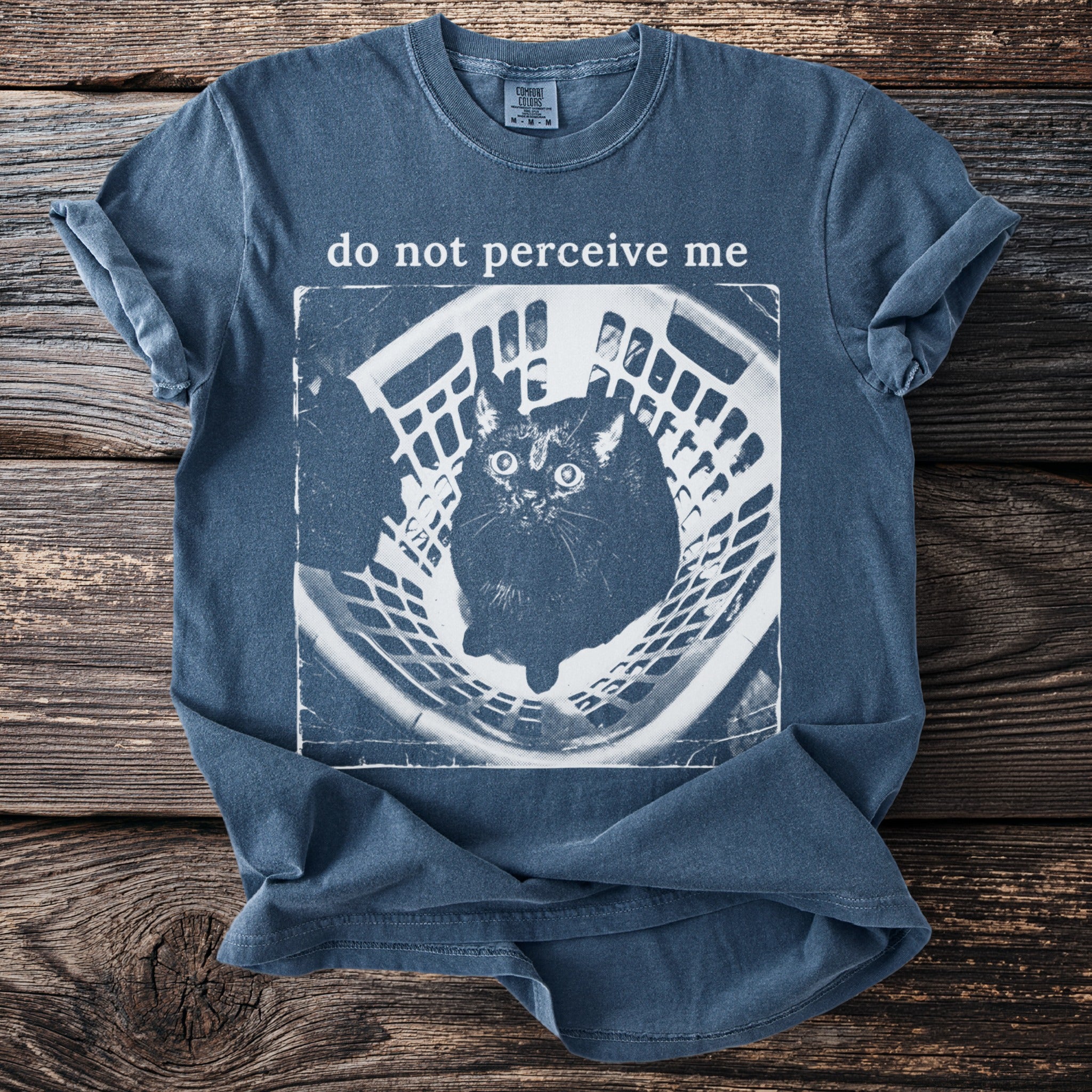 Blue t-shirt with "do not perceive me" text and a cat in a basket graphic.