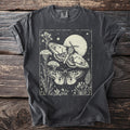 Dark grey t-shirt with a light cream graphic of two moths, a moon, and plants.