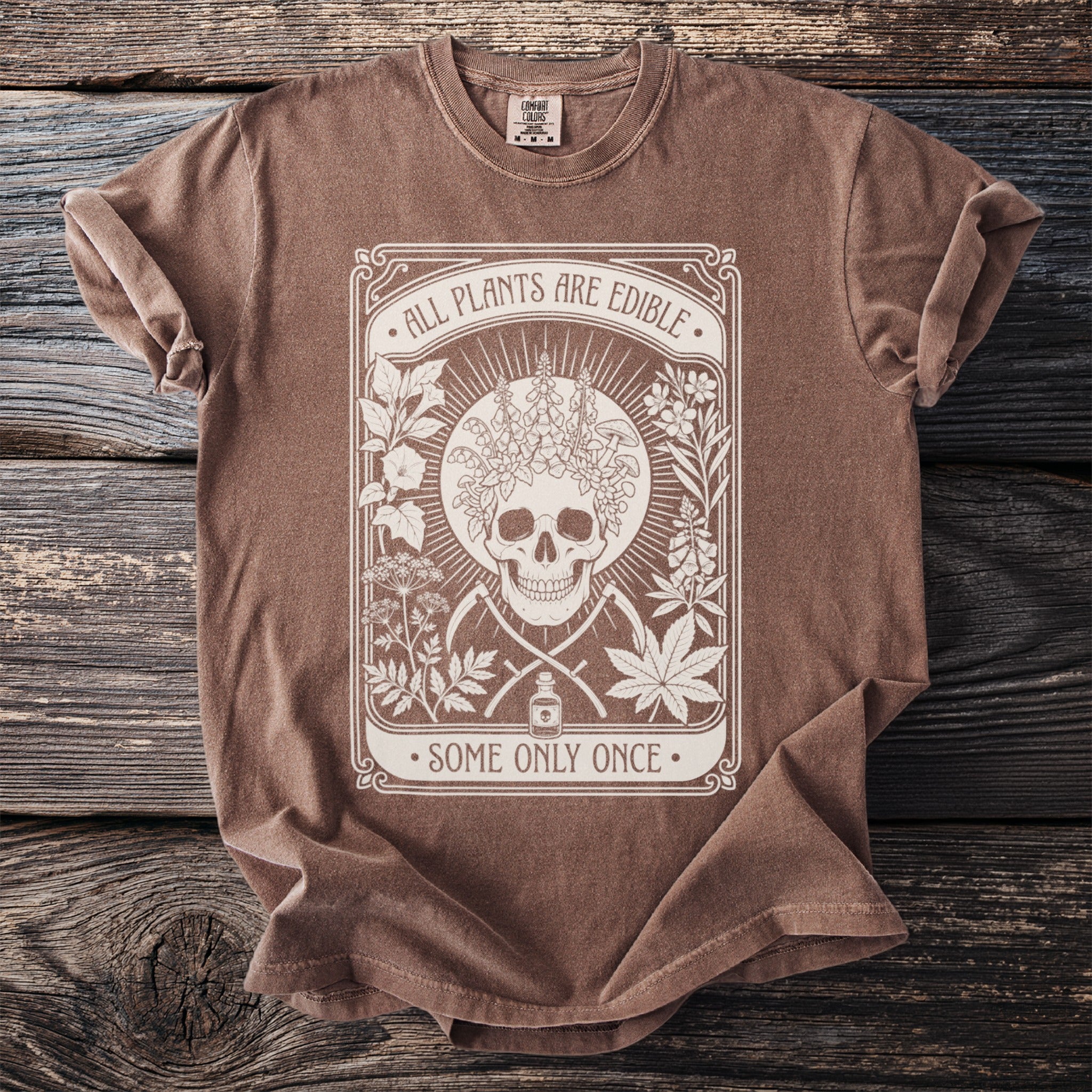 Brown t-shirt with white graphic of skull, plants, and text: ALL PLANTS ARE EDIBLE. SOME ONLY ONCE.