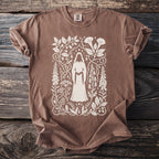 Brown t-shirt with white graphic of hooded figure and botanical elements.