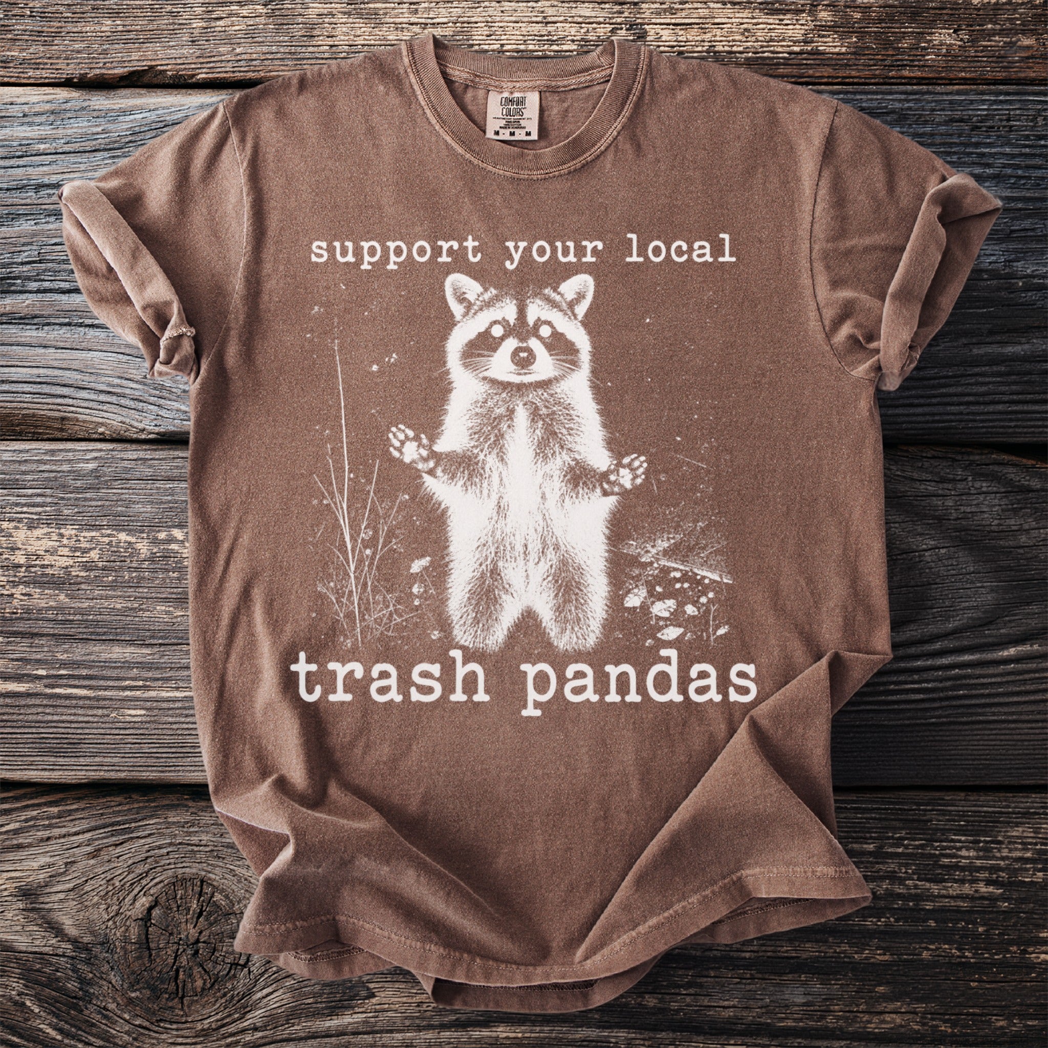 Brown t-shirt with graphic of raccoon and text "support your local trash pandas".