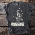 Pepper gray t-shirt with a cream folk-cut print: Krampus sits on a three-legged stool on the ice, a fishing line down a small hole.