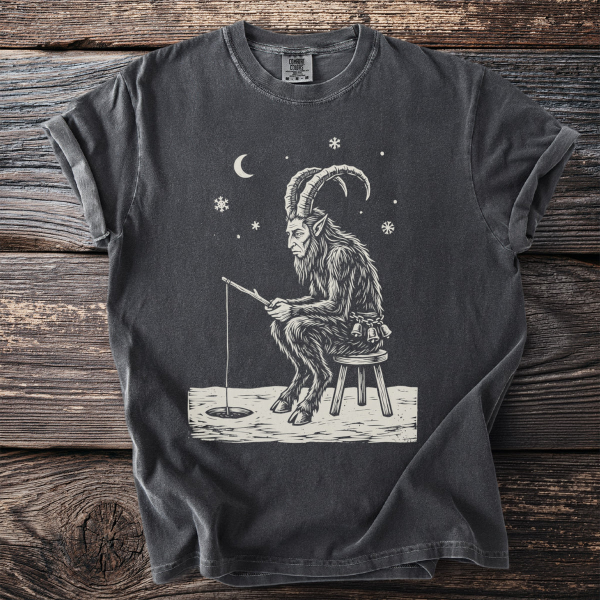 Pepper gray t-shirt with a cream folk-cut print: Krampus sits on a three-legged stool on the ice, a fishing line down a small hole.