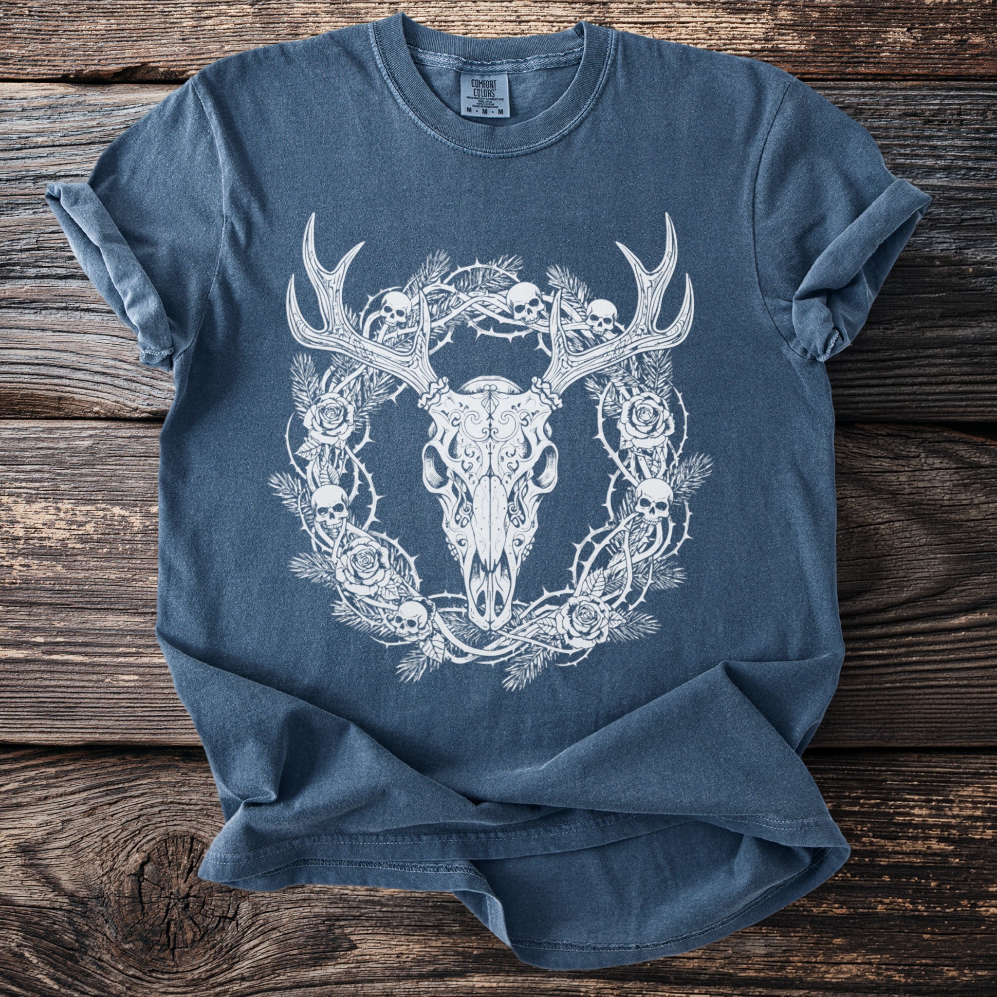Blue t-shirt with a white illustration of a deer skull, thorny branches, skulls, and roses.