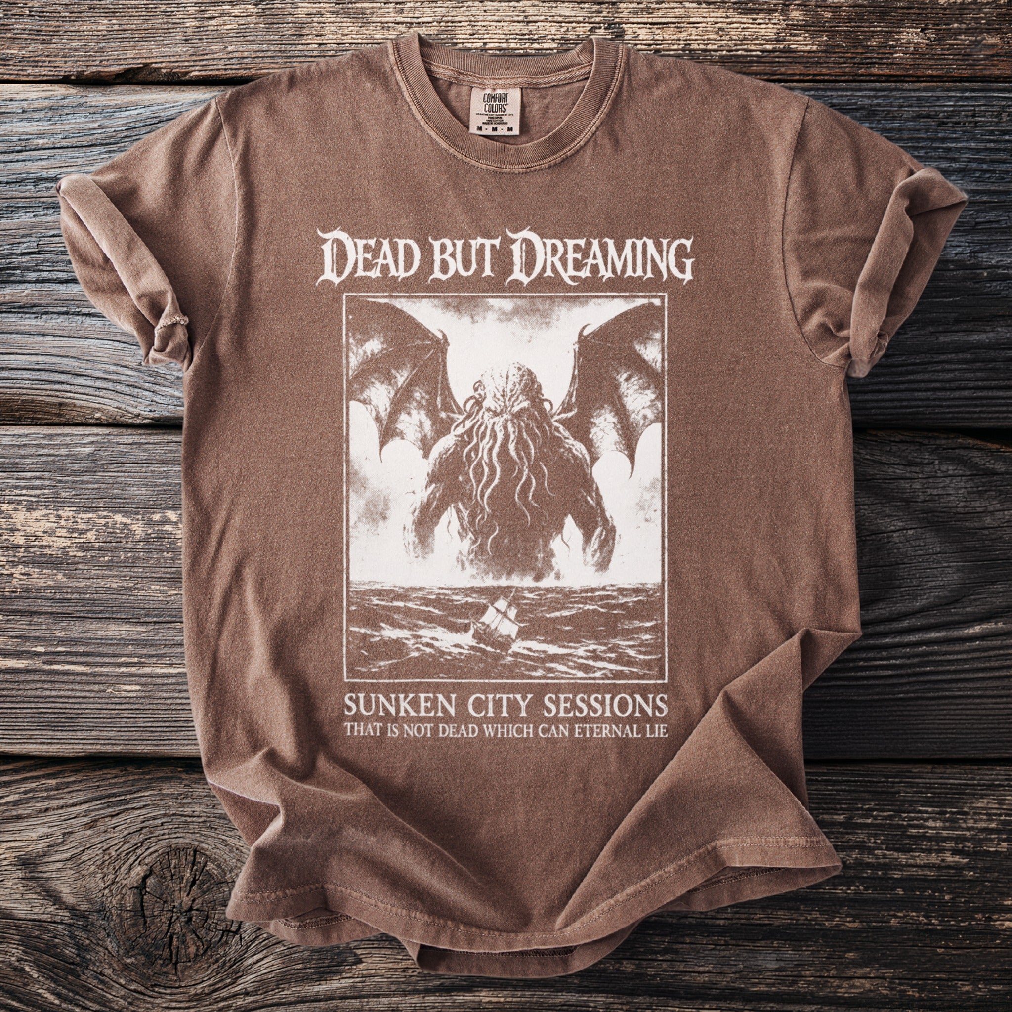 Brown t-shirt with "Dead But Dreaming" and tentacled creature graphic.