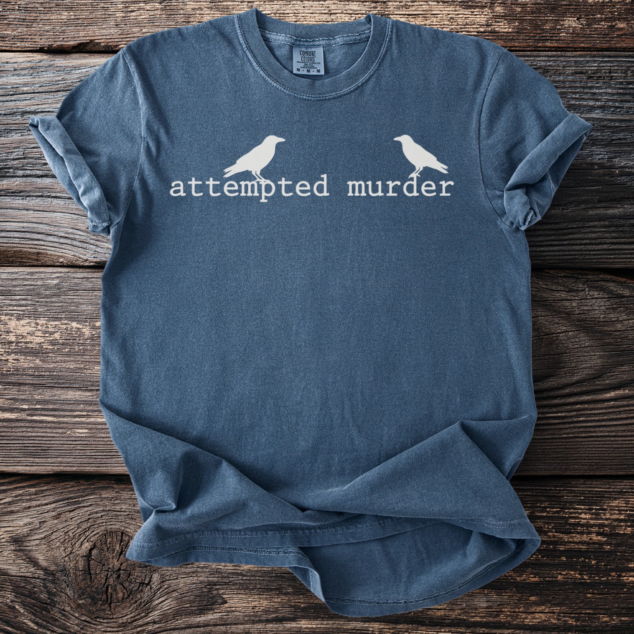 Blue t-shirt with white text "attempted murder" and two birds.