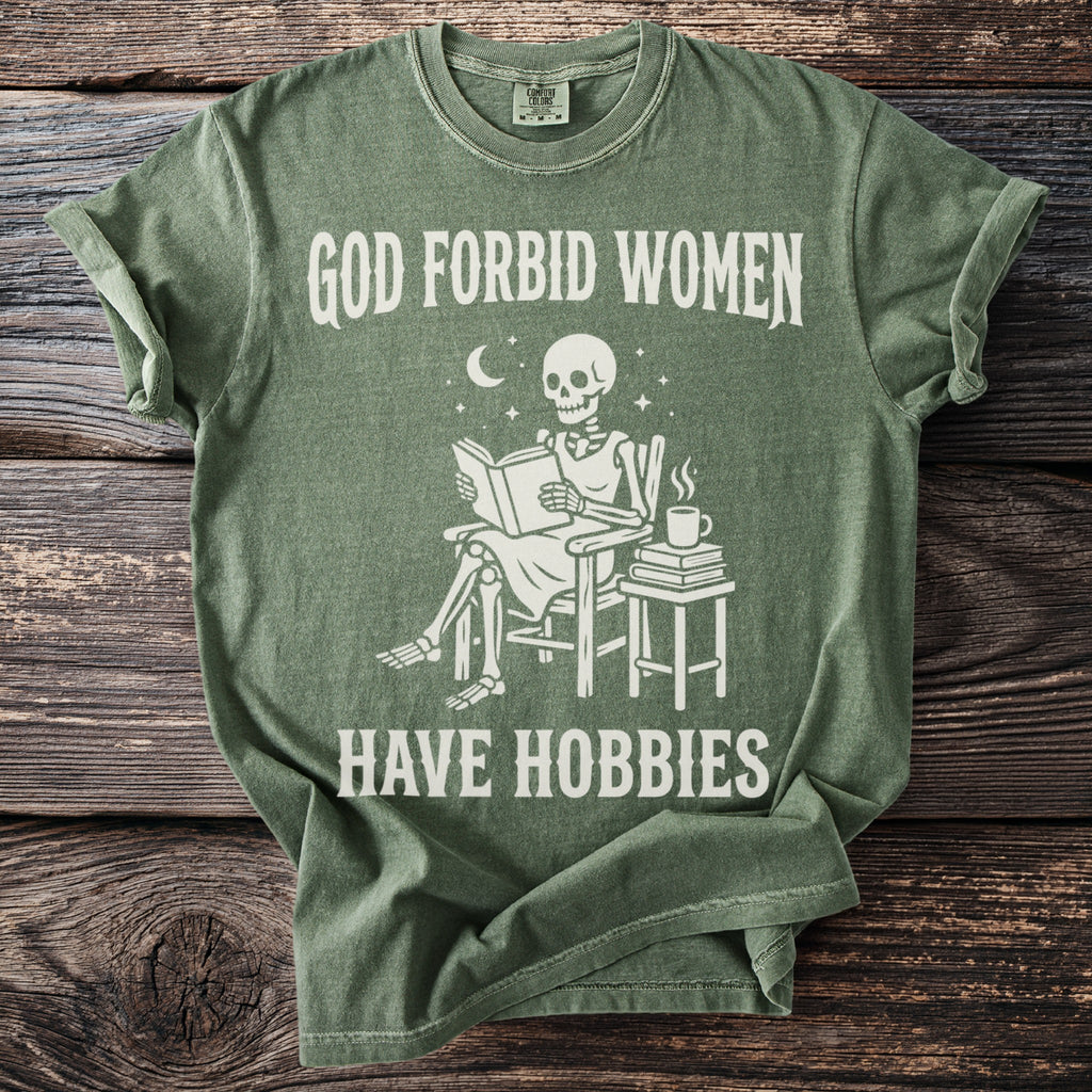 Green t-shirt with skeleton reading a book on chair, "GOD FORBID WOMEN HAVE HOBBIES".