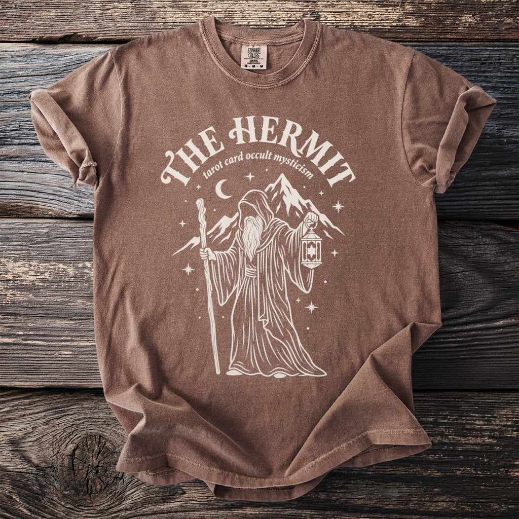 Brown t-shirt with white graphic of "The Hermit" tarot card, a robed figure with a lantern.
