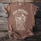 Brown t-shirt with white graphic of "The Hermit" tarot card, a robed figure with a lantern.