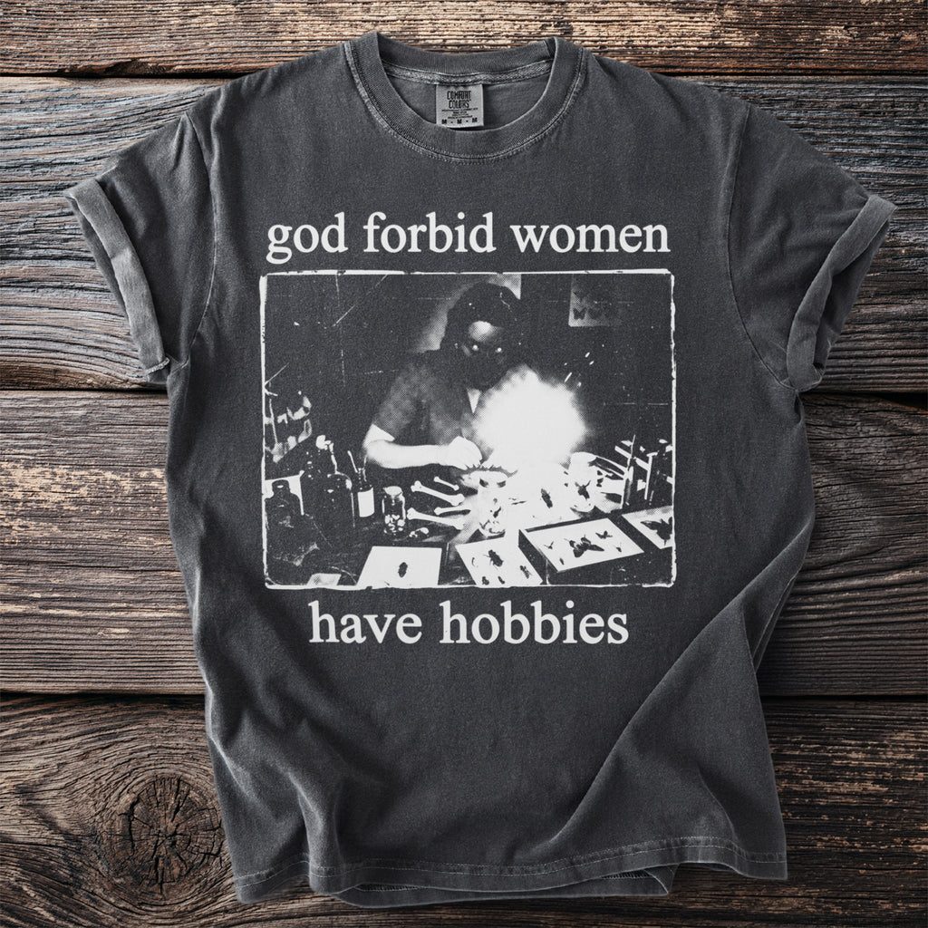 Dark grey t-shirt with text "god forbid women have hobbies" and a vintage scientific illustration.