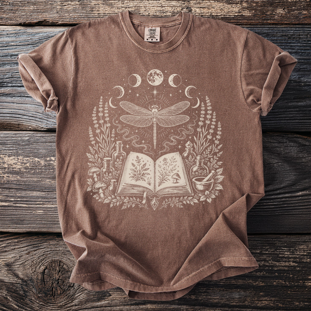 Brown t-shirt with a mystical design of a dragonfly above an open book.