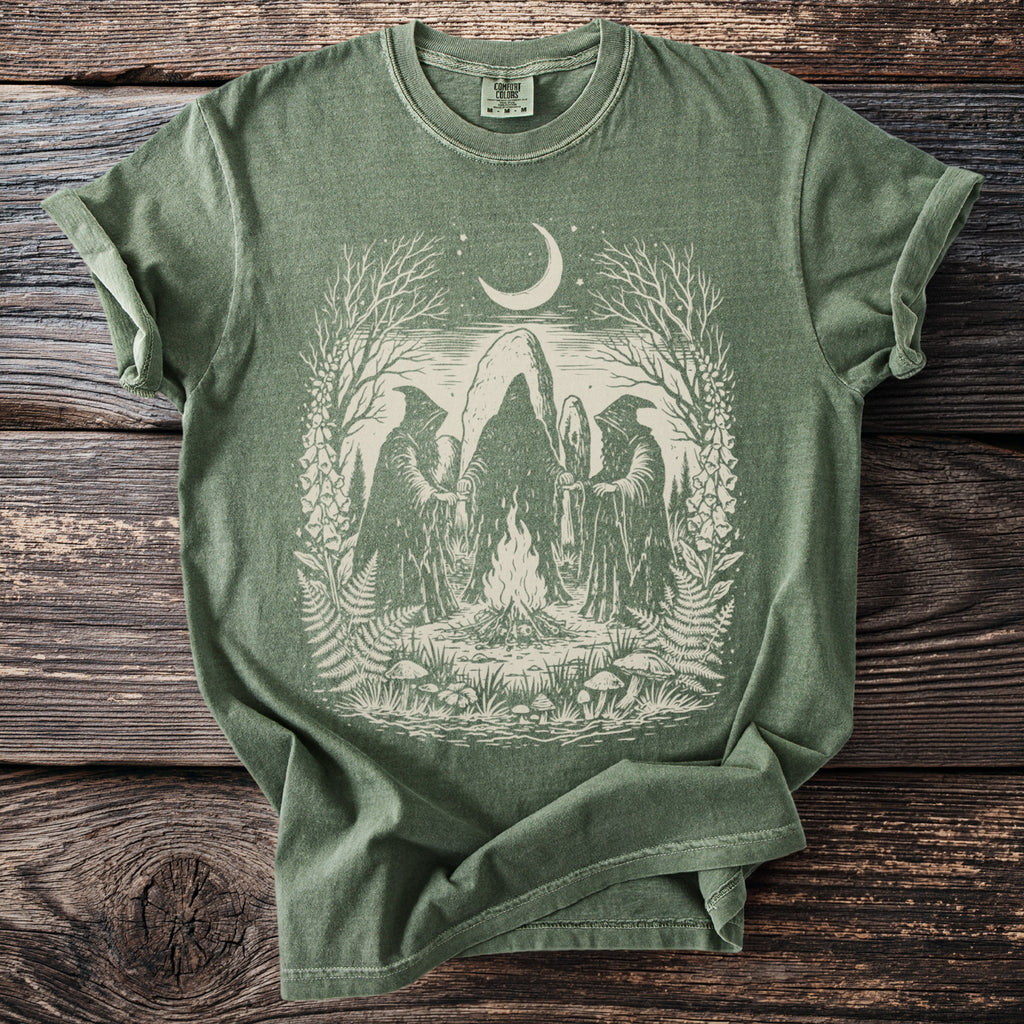 Green t-shirt with graphic of figures in robes around a campfire under a crescent moon.
