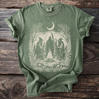 Green t-shirt with graphic of figures in robes around a campfire under a crescent moon.