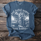 Blue t-shirt with graphic "god forbid women have hobbies" and illustration.