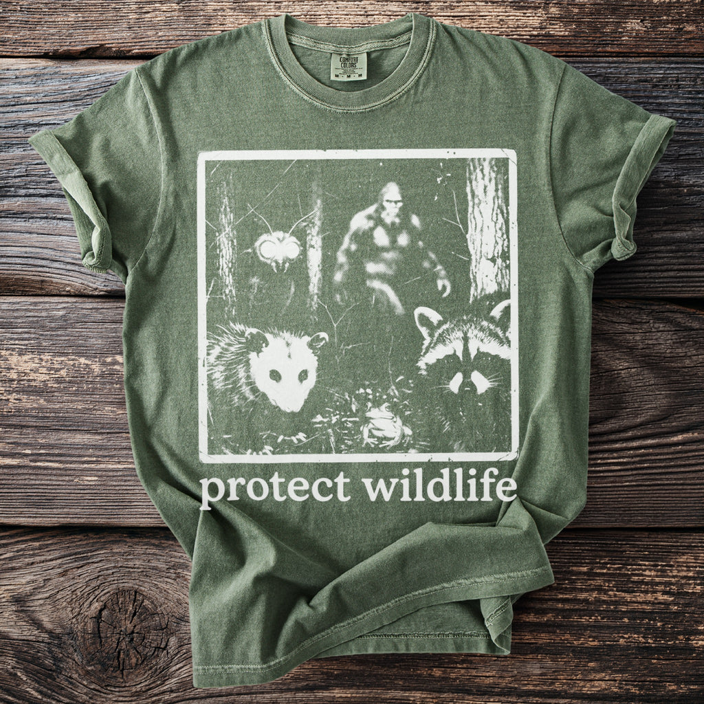 Green t-shirt with graphic of Bigfoot, possum, raccoon, and insect with "protect wildlife" text.