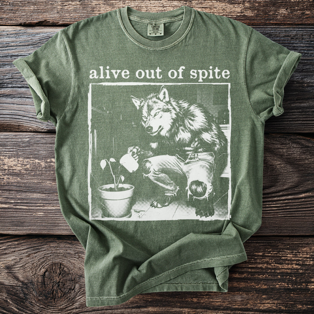 Green t-shirt with "alive out of spite" text and wolf watering a plant graphic.