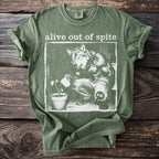Green t-shirt with "alive out of spite" text and wolf watering a plant graphic.