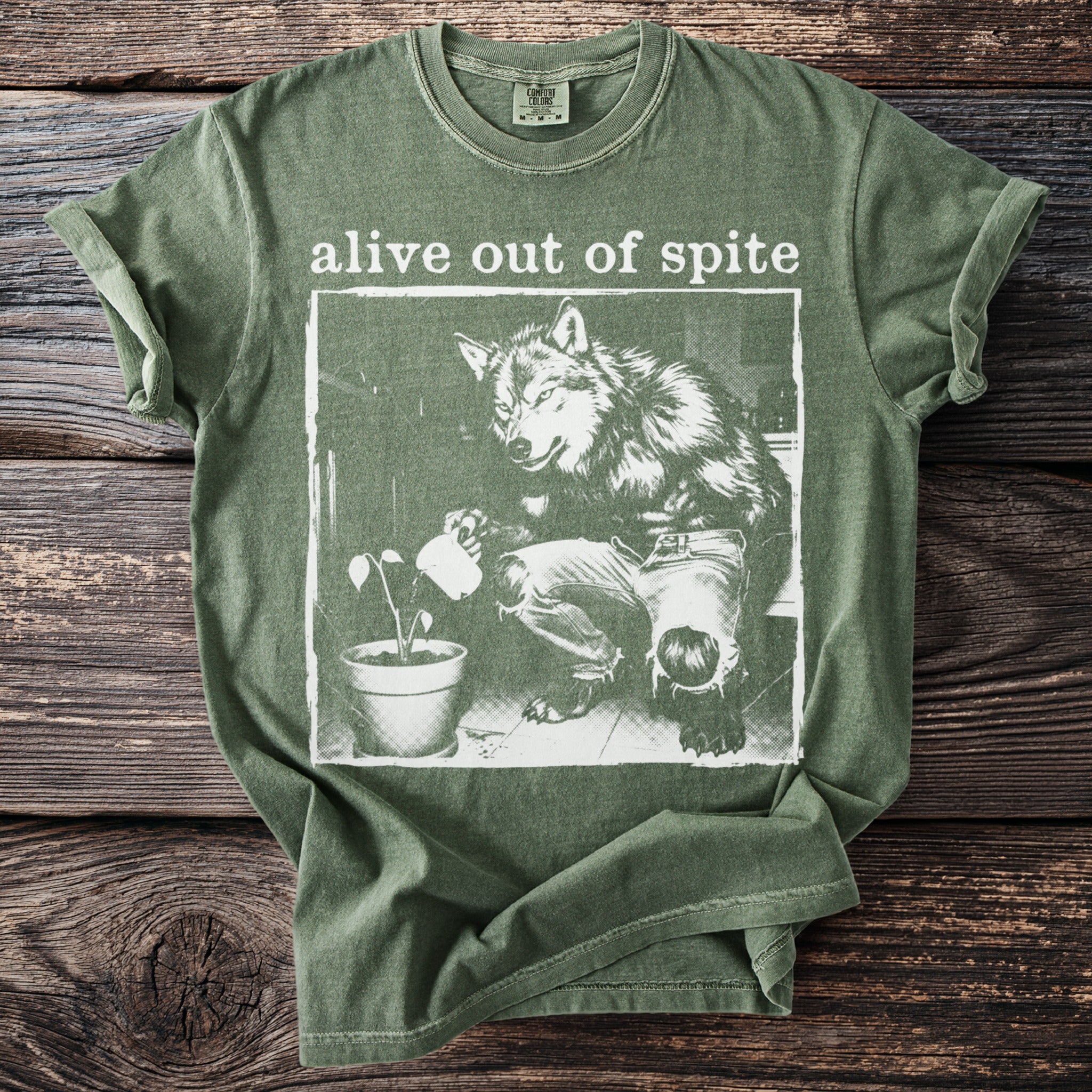 Green t-shirt with "alive out of spite" text and wolf watering a plant graphic.