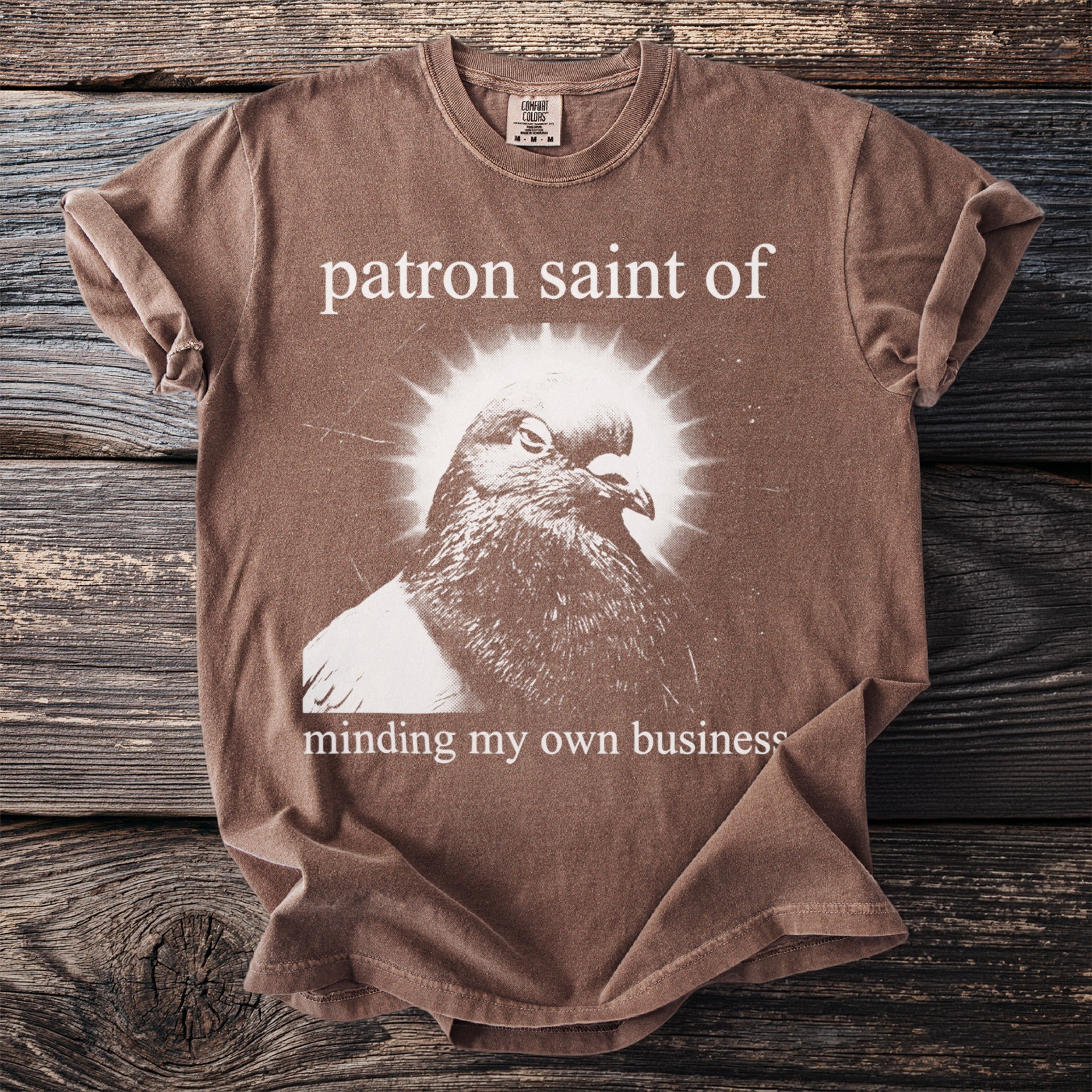Brown t-shirt with "patron saint of minding my own business" and a pigeon graphic.