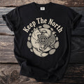 Black t-shirt with cream graphic of fox, bird, compass, and pinecones, text "Keep The North".