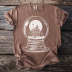Brown t-shirt with white graphic of a haunted house inside a snow globe.