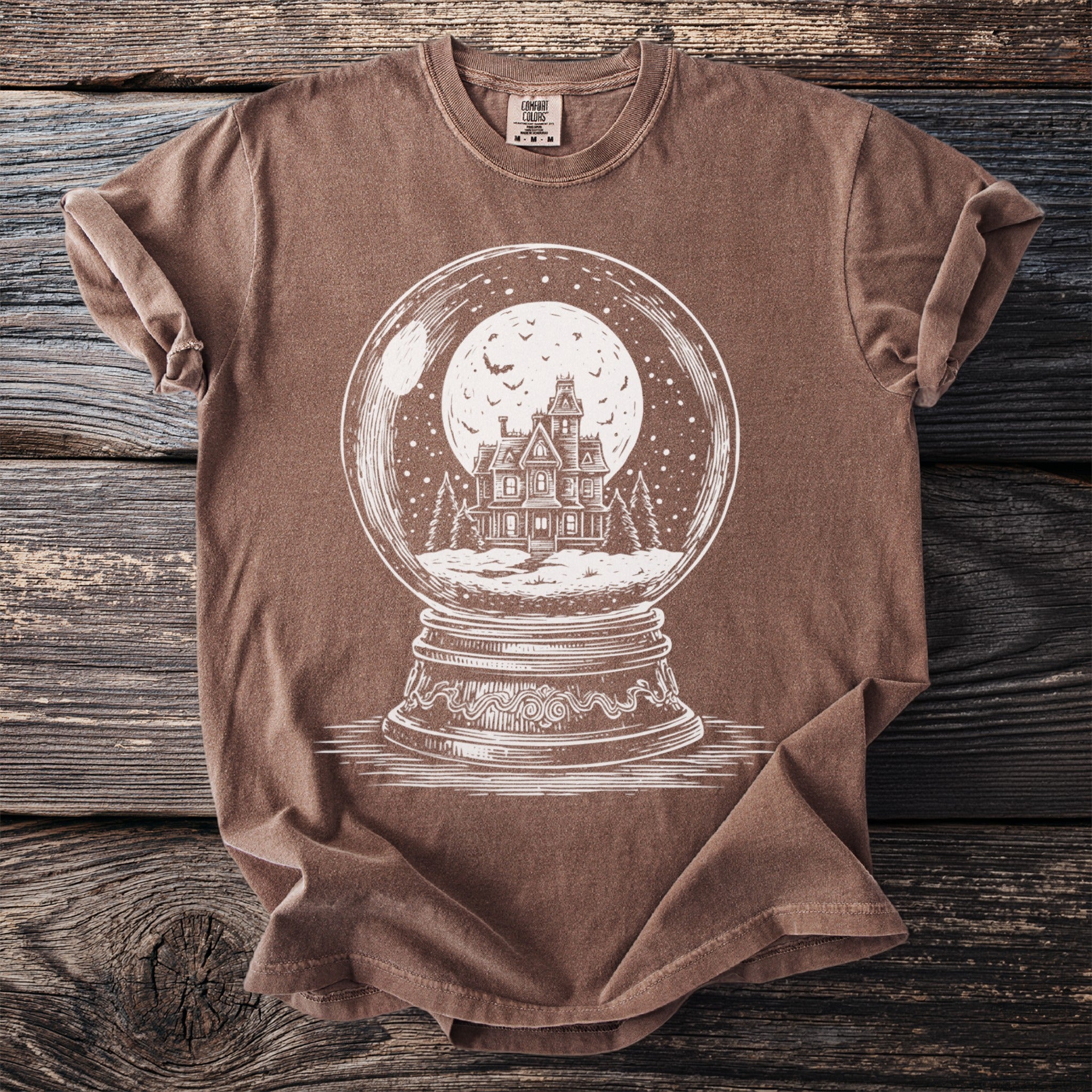 Brown t-shirt with white graphic of a haunted house inside a snow globe.
