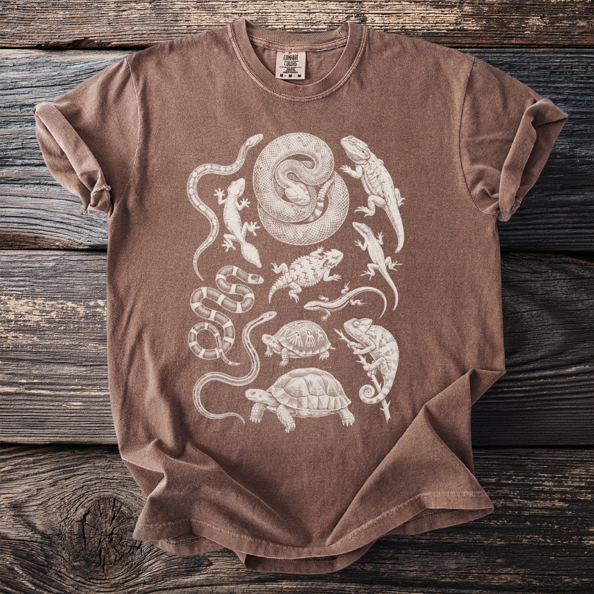 Brown t-shirt with a detailed white line drawing of various reptiles and amphibians.