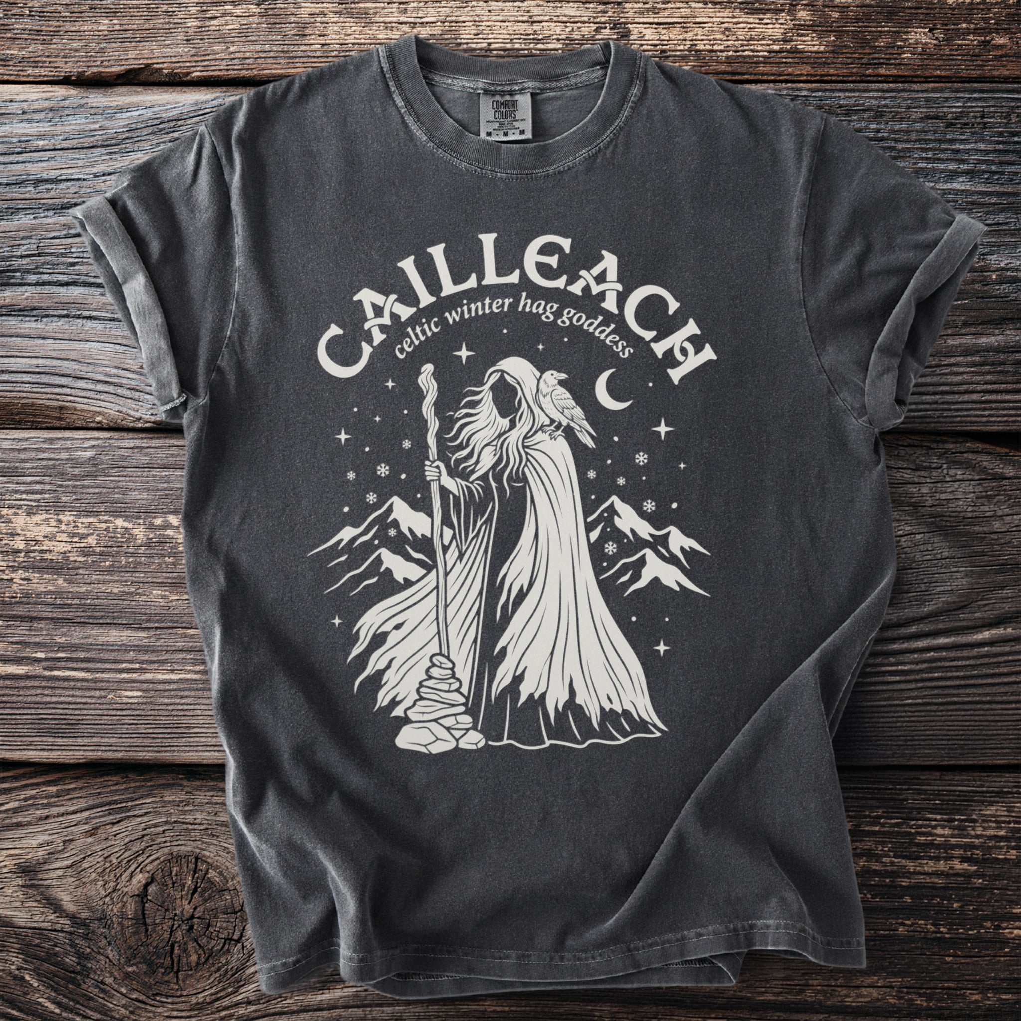 Cailleach celtic winter hag goddess with raven and mountains graphic on a dark gray t-shirt.