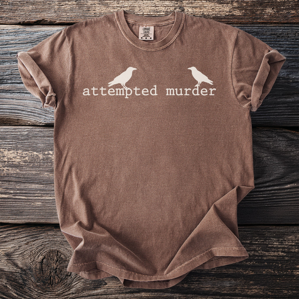 Brown t-shirt with white text "attempted murder" and two crow silhouettes.