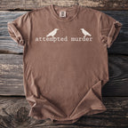 Brown t-shirt with white text "attempted murder" and two crow silhouettes.