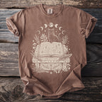 Brown t-shirt with a white line drawing of a cat, moon phases, and an open spell book.