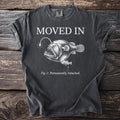 Dark t-shirt with "MOVED IN" and anglerfish illustration with text "Fig. 1: Permanently Attached."