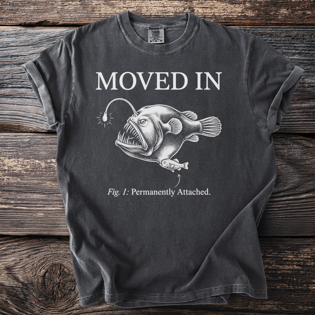 Dark t-shirt with "MOVED IN" and anglerfish illustration with text "Fig. 1: Permanently Attached."