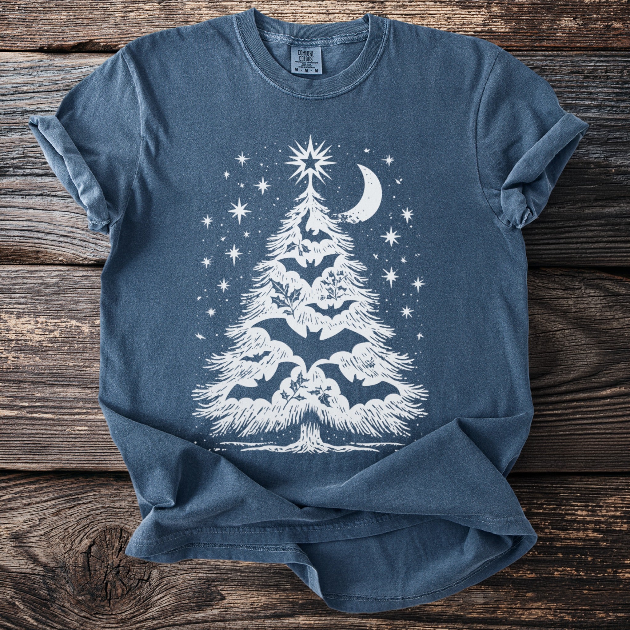 Blue t-shirt with white Christmas tree graphic featuring bats and holly under a crescent moon.