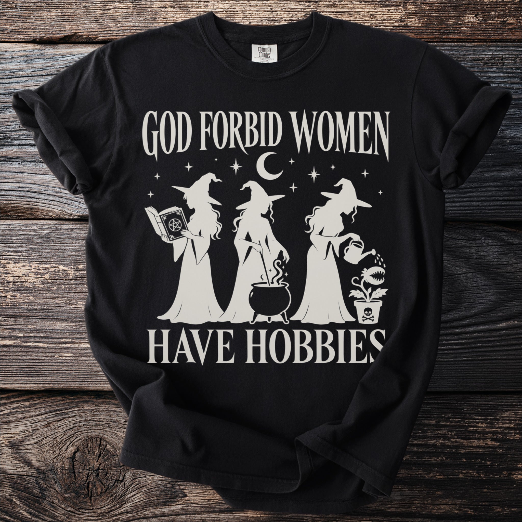 Black t-shirt with "God Forbid Women Have Hobbies" text and witch graphics.
