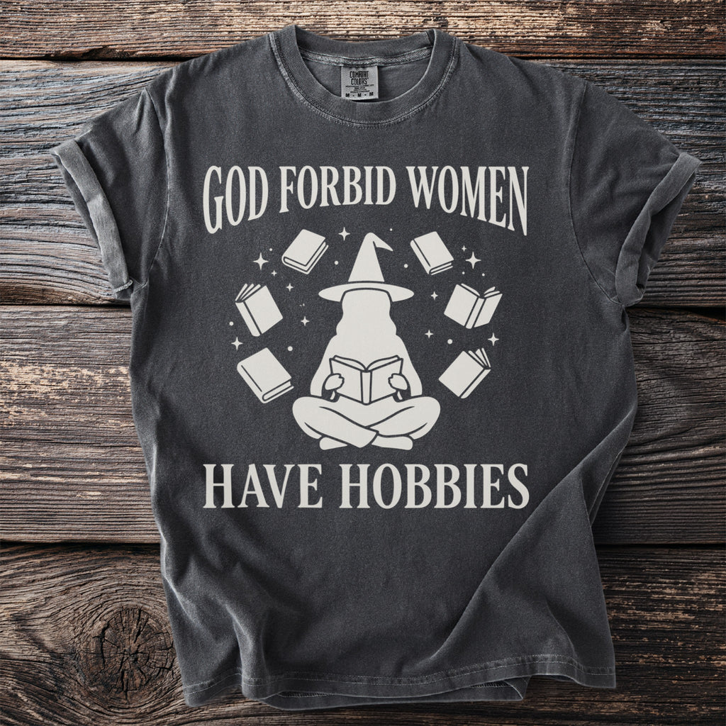 T-shirt with text "God forbid women have hobbies" and a graphic of a witch reading surrounded by books.