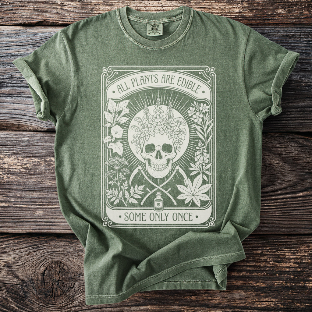 Green t-shirt with skull, plants, scythes, potion bottle, and text "All Plants Are Edible, Some Only Once."