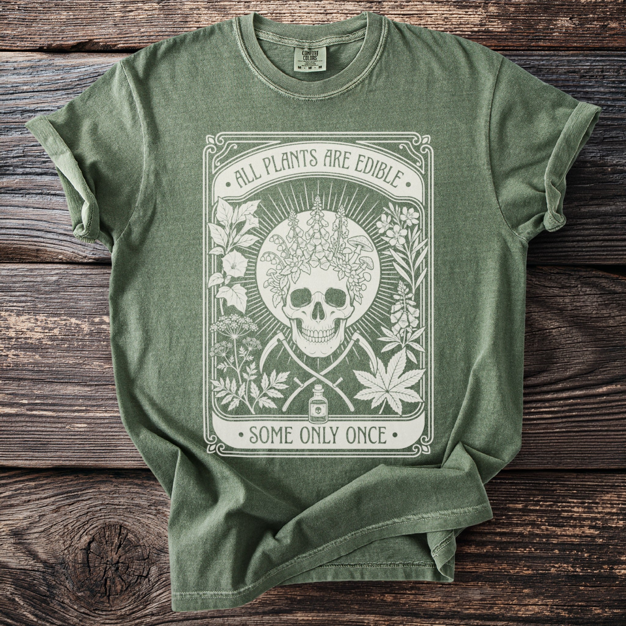 Green t-shirt with skull, plants, scythes, potion bottle, and text "All Plants Are Edible, Some Only Once."