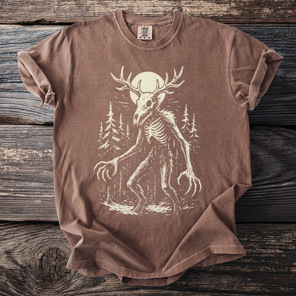 Brown t-shirt with a skeletal creature and moon graphic in a forest.